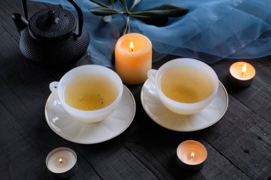 İki beyaz fincan, siyah masa ve mumlar.