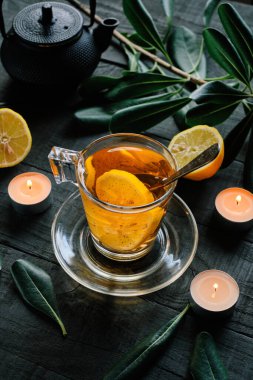 Siyah bir masada limon dilimleri ve mumlarla bir fincan çay.