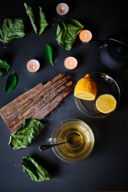 Yeşil çay fincanı, tütsü çubuğu, mumlar ve limonlar siyah masada.