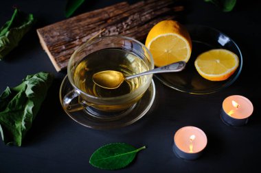 Yeşil çay fincanı, tütsü çubuğu, mumlar ve limonlar siyah masada.