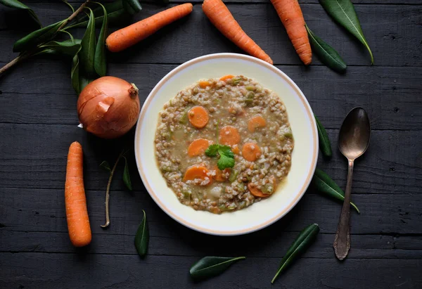 Plate of cooked lentils with carrot, onion and pepper on black table