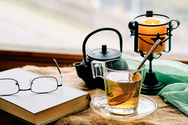 Yeşil çay fincanı, kitap ve mum pencerenin yanında.