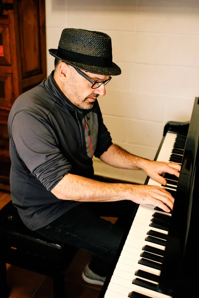 Mature pianist with hat playing the piano in his studio