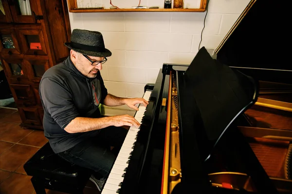 Mature pianist with hat playing the piano in his studio