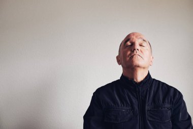 Gri duvarda gözleri kapalı orta yaşlı bir adam.