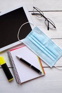 Ameliyathane maskesi, tablet, gözlük, not defteri ve kalem.