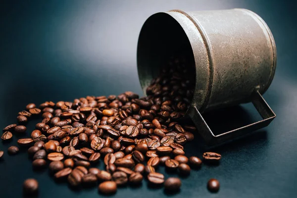 Siyah arka planda kahve çekirdekleri olan eski metal bardak.