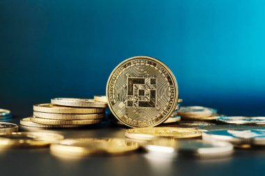 Önde gelen bir Binance madeni parası, altın tonlarını vurgulayan çarpıcı mavi bir arka planla yakın plan görüntüsünde diğer madeni parlaklıklar arasında parlar..
