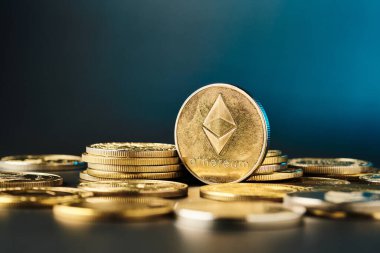 Önde gelen bir ethereun sikkesi, altın tonlarını vurgulayan çarpıcı mavi bir arka planla, diğer madeni paralar arasında parlak bir şekilde parlar..