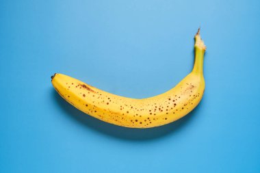 Kahverengi benekli olgun sarı bir muz canlı mavi bir arka planda duruyor ve tazeliğini gösteriyor. Hızlı ve besleyici bir ikram ya da kahvaltı için ideal..