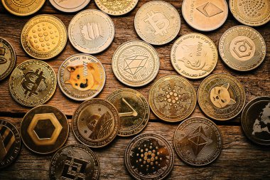 Farklı kripto paralar ahşap bir masada düzenlenir. Her sikke Bitcoin ve Ethereum gibi çeşitli dijital para birimlerini temsil eden eşsiz dizayn ve sembollere sahiptir..