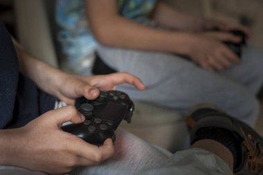 Çocuk evdeki kanepede oturup dizüstü bilgisayarında video oyunu oynarken joystick tutuyor.