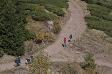 Kırmızı ve mavi ceketli iki motorcu dağ yolunu araştırıyor. Yükseklikten iki motor sürücüsüne bakıyor.
