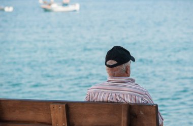 Yaşlı bir adam, bir dede, siyah şapkalı yaşlı bir emekli denize bakıyor. Üst düzey bir adam açık bir bankta oturuyor ve manzaranın tadını çıkarıyor..