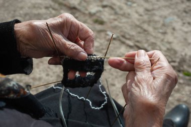 Yaşlı kadın çorap örüyor. Yaşlı büyükanne parkta dinleniyor, yeni doğan torun ailesi için örgü örüyor.