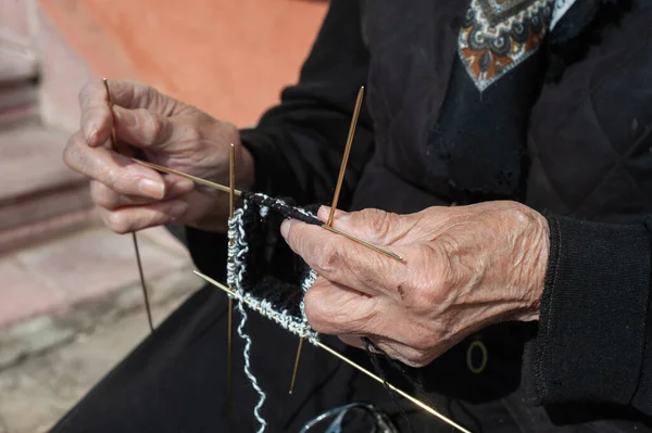 Hands of elderly woman knitting sock.Old grandmother resting on bench in park, knitting for newborn grandchild family