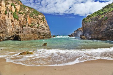 Manzara okyanus dalgalarının plaja kayaların arasında. Güneşli bir gün, yüksek kayalar sağ ve sol, dalgalar deniz kumlu sahilde çalıştırın.