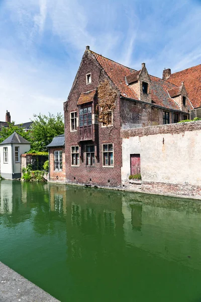 Ancient houses on the bank of the channel in Bruges, Belgium. Houses from a brick and a stone, with tile roofs. Summer sunny day, reflection in water of the channel.