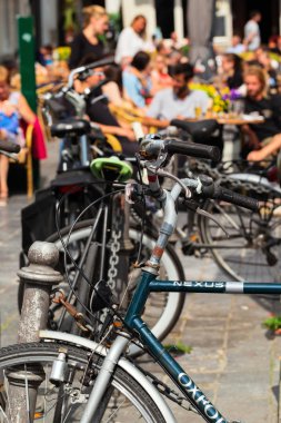 Bruges, Belçika - 8 Haziran 2017: Bisikletler kümesi sokak café'de park etmiş. Küçük tablolar arkasındaki insanlar ön planda odak bisiklet bir dinlenme var. Güneşli yaz günü, tempolu sokak