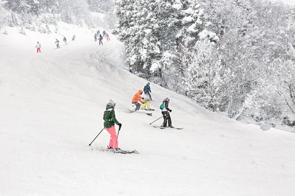 Downhill skiing during a heavy snowfall. Group of tourists, adults and children, on a resort slope in Andorra.