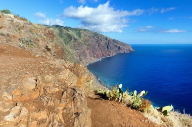 Madeira Adası batı kısmından okyanus manzaralı. Taşlar, seyrek bitki örtüsü ve güneşli yaz gününde mavi su