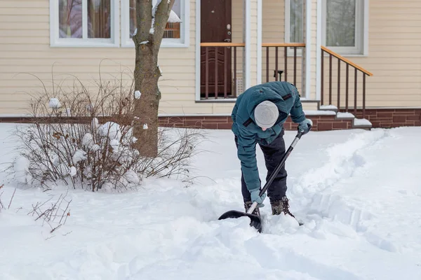 Ein Mann beseitigt Schnee in der Nähe eines Landhauses, räumt den Weg — Stockfoto