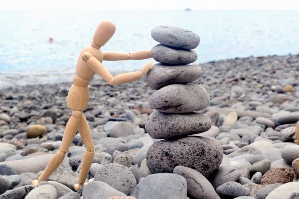 A figura de um homem de madeira constrói uma pirâmide de pedras na praia . — Fotografia de Stock