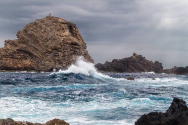 Yüksek bir yalnız kayanın arka planına karşı okyanus kıyısında fırtına dalgaları