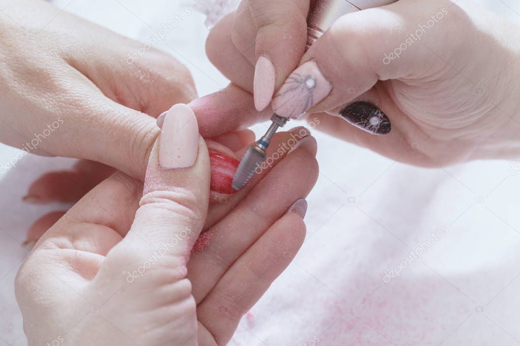 The hands of the master of the hardware manicure and the hands of the client close-up during the preparatory work.