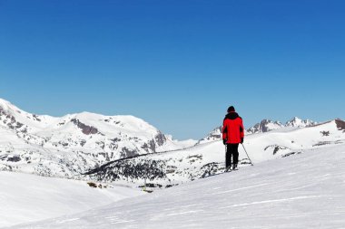 Pireneler, Andorra - 14 Şubat 2019: Parlak kırmızı ceketli bir kayakçı güneşli bir kış gününde bir dağın tepesinde duruyor