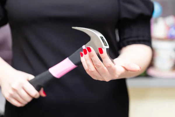 Kadınların elleri, tehdit edici veya kararsız bir pozisyonda pembe saplı büyük bir çekiç tutar.