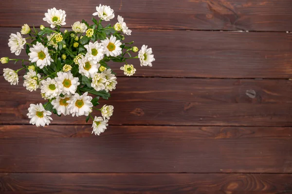 A bouquet of white bush chrysanthemums on a wooden table in the upper left corner. — Stock Photo, Image