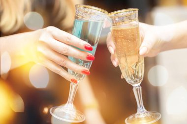 Şenlik arka planında şampanya kadehleri olan iki kadın eli..