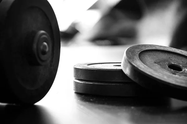 Fitness workout equipment. Dumbbell or barbell on a wooden floor surface. Black and white picture