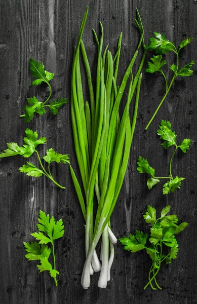 Cooking concept: Fresh green onion and culinary parsley on black desk top view flat lay