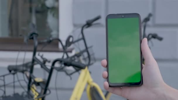 Vrouwelijke handen houden zwarte smartphone met groen scherm op straat BG. — Stockvideo