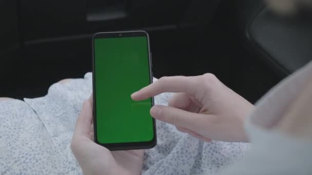 Close-up van de hand van een vrouw met een mobiele telefoon groen scherm in de auto — Stockvideo