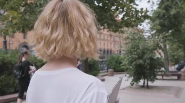 Şehir caddesinde yürüyen genç bir iş kadınının dikiz görüntüsü. Yavaş çekim.