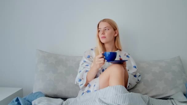 Giovane ragazza beve caffè o tè e guarda fuori dalla finestra. — Video Stock