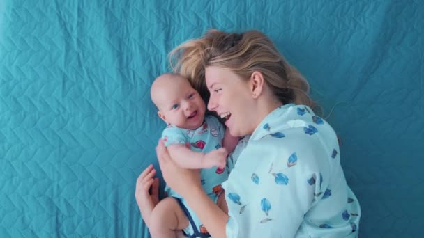 Genç bir anne bebeğiyle yatakta uzanıyor ve eğleniyor.. — Stok video