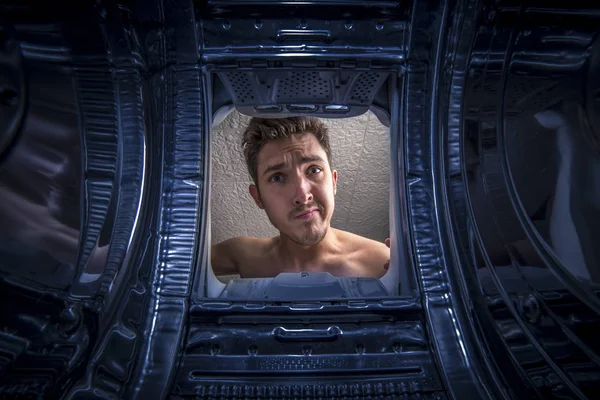 Young man doing laundry View from the inside of broken washing machine