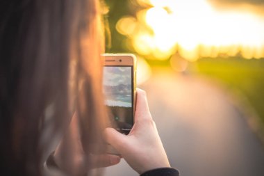 Gün batımında onun smartphone ile fotoğraf çekmeye kadın