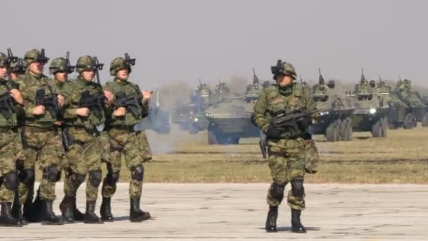 Сербия Марширующие солдаты в миметической униформе с бронированными транспортными средствами на заднем плане — стоковое видео