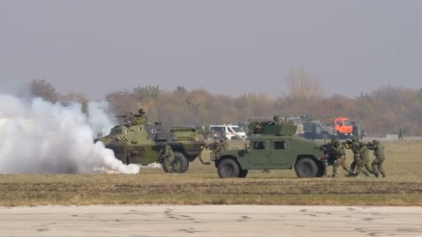 Des soldats marchent couverts d'une voiture militaire humvee et fument sur le champ de bataille — Video