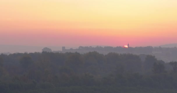 Timelapse El sol se levanta detrás del campanario de la iglesia entre los árboles a amplia vista — Vídeos de Stock