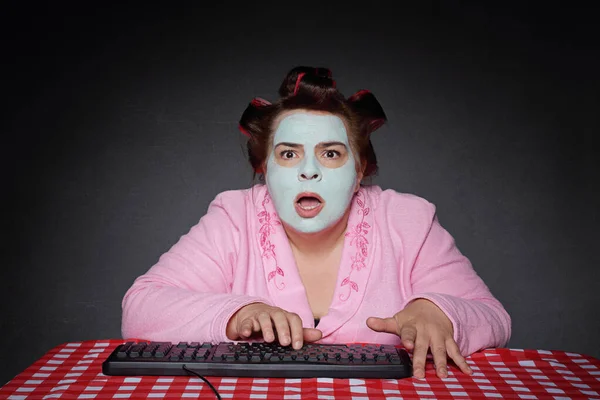 funny overweight fifty year old woman wearing bathrobe and face mask getting frustrated on bugging laptop pc on studio grey background