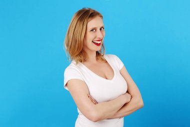 Genç ve beyaz tenli sarışın kadın mavi izole stüdyo arka planında gülümsüyor.