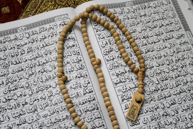 Kutsal Kur 'an, tespih ya da hasırın üzerindeki tasbih. Müslümanların kutsal kitabı Kur 'an, kahverengi dua paspasının üzerine konur. Kutsal El-Kur 'an ve Arapça yazı..