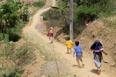 Çocuklar tarlaların ortasındaki köy yolunda çeşitli bitkilerle yürüyorlar. Sukawangi bölgesindeki doğal manzara ve köy yolları, Bogor, Endonezya. 6 Eylül 2020