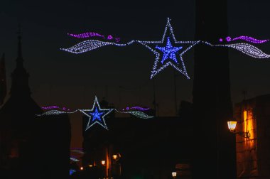 Noel ışıkları, mavi yıldız şekilleri, sokaklarda asılı.